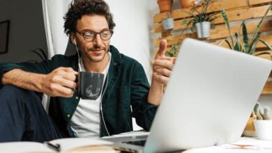 Un homme en train de faire du télétravail devant son ordinateur, tasse de café à la main