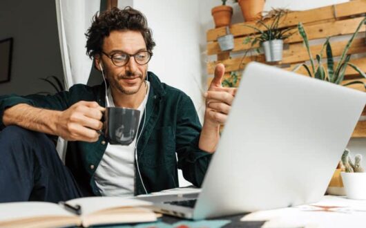 Un homme en train de faire du télétravail devant son ordinateur, tasse de café à la main