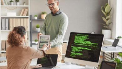 Une femme face à un écran de code échange avec un collaborateur