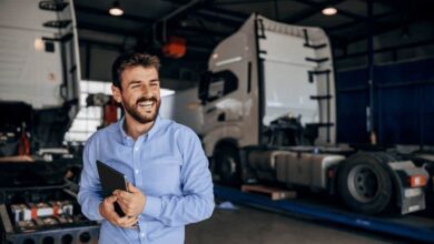 Un homme souriant dans le dépôt d'une entreprise de transport, avec deux camions en arrière-plan