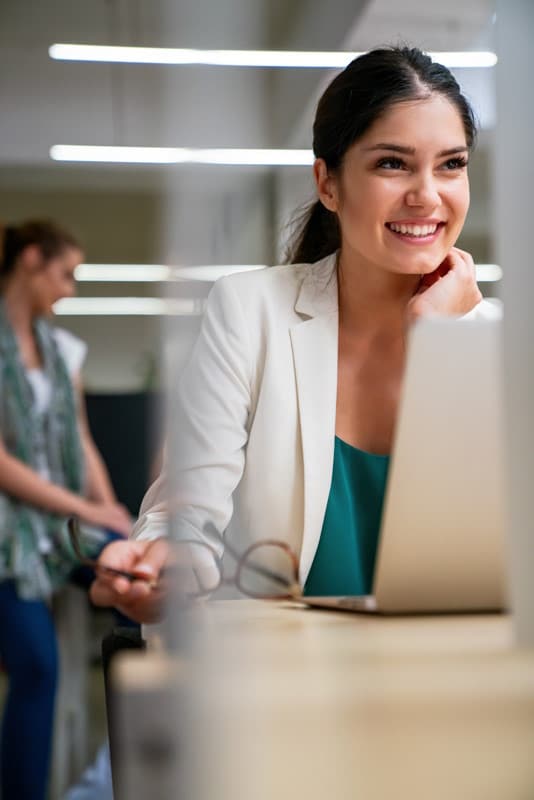 Une femme sourit devant son ordinateur, bénéficiant des nombreuses fonctionnalités du logiciel Silae